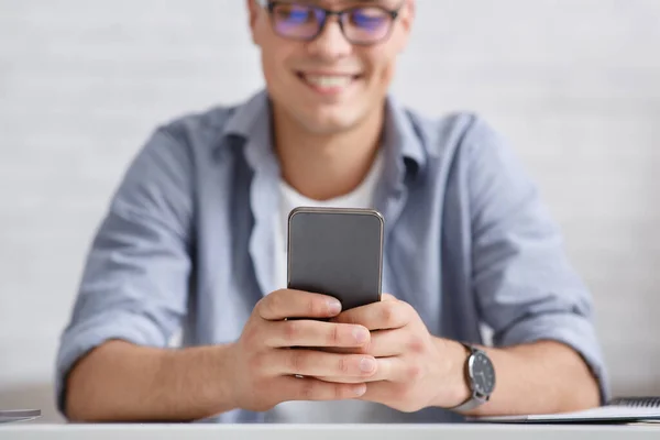 Sorrindo cara com óculos olha para o telefone, foco no smartphone — Fotografia de Stock