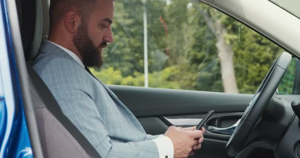 Серьезный бизнесмен пишет смс на смартфоне в машине, сидит на водительском сидении — стоковое видео