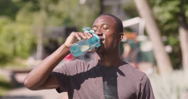 Втомлений, але щасливий афроамериканський спортсмен п'є воду після напруженого тренування в міському парку — стокове відео