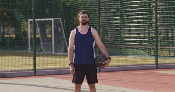 Стритболист, стоящий с баскетбольным мячом на открытой площадке — стоковое видео