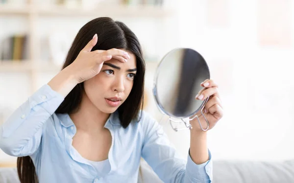 Problemhud. Orolig asiatisk kvinna tittar i rund spegel och rörande panna — Stockfoto