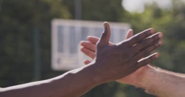 Beyaz ve Afrikalı erkekler açık hava basketbol sahasında birlik sembolü olarak el ele tutuşuyorlar.