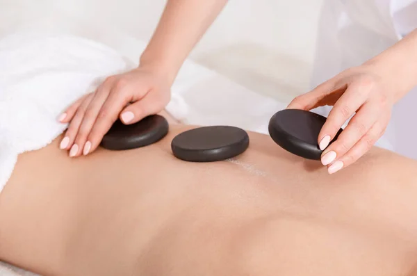 Tratamentos de spa para a beleza. As mãos colocam pedras quentes na mulher de volta na mesa de massagem — Fotografia de Stock