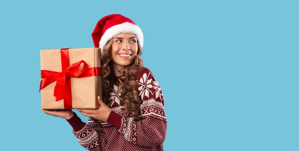 Faire du shopping pour Noël. Douce jeune fille dans le chapeau Santa avec boîte cadeau en regardant l'espace vide sur fond bleu — Photo