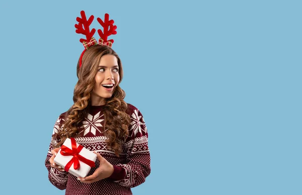 Sexy chica en suéter caliente celebración de regalo de Navidad y mirando el espacio vacío, fondo azul — Foto de Stock