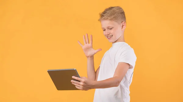 Mutlu okul çocuğu video çağrısı ve el sallama için tablet kullanıyor. — Stok fotoğraf