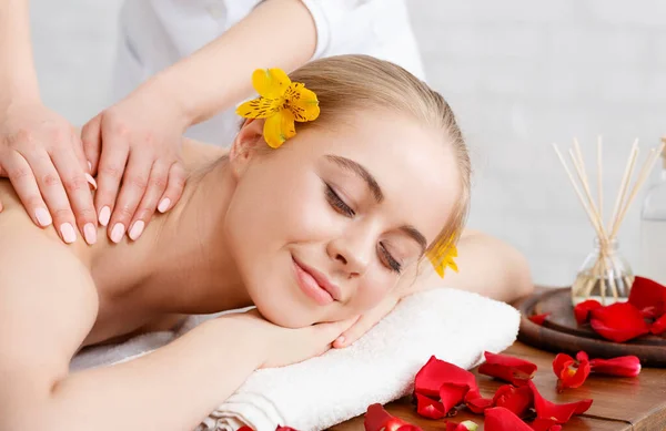 Relaxe e cuidados de beleza. Menina sorridente encontra-se na mesa de massagem com pétalas de flores — Fotografia de Stock