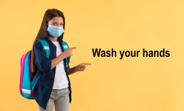 Maskeli çocuk ellerini yıka mesajını işaret ediyor.