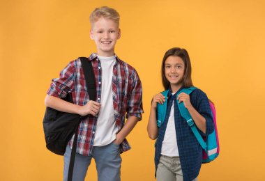 Stüdyo arka planında okul çantalarıyla poz veren öğrenciler