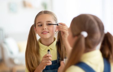 Makyaj yapan, maskarayı süren, aynaya bakan bir kız.
