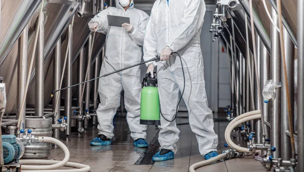 Trabajadores en trajes de protección con bolsa de aerosol y tableta en fábrica — Foto de Stock