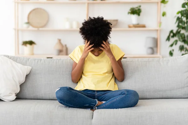 Infeliz negra chica tocando la cabeza sentado en sofá en casa — Foto de Stock