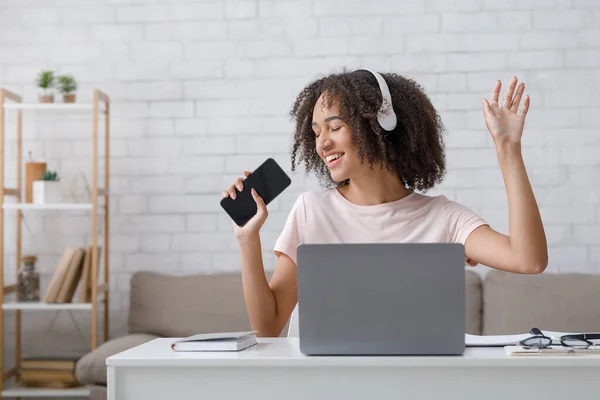 Tempo libero dopo le lezioni online. Allegro afroamericano ragazza in cuffia cantare in smartphone — Foto Stock