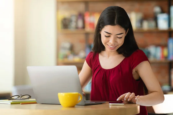 Beskjed fra Asiatisk jente på smarttelefon mens hun jobbet på en laptop på kafe – stockfoto