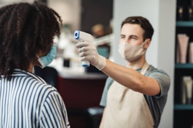 Güzellik hocası salonda bayan müşterinin ateşini ölçüyor.