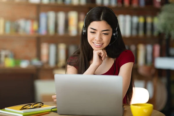 Alegre coreana chica en auriculares viendo webinar a través de ordenador portátil en el café —  Fotos de Stock