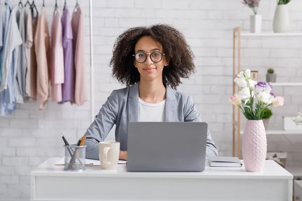 Startup en mode bedrijf. Vriendelijk Afrikaans amerikaanse vrouw in bril zitten aan tafel met laptop — Stockfoto