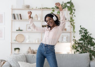 Neşeli ruh hali. Mutlu kız kulaklıkla müzik dinliyor ve evde dans ediyor.