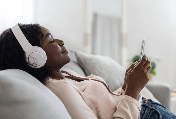 Calma donna africana rilassante con smartphone e cuffie a casa, Ascoltare musica — Foto Stock