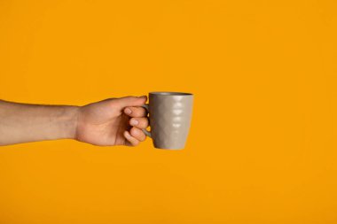 Turuncu arka planda, erkek eli, lezzetli bir bardak sıcak içecek, yakın plan.