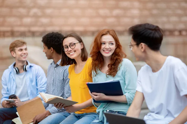 Wesoła licealiści rozmawiający podczas przerwy siedzi i uczy się na świeżym powietrzu — Zdjęcie stockowe