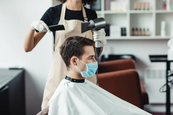 Jovem em máscara protetora recebendo corte de cabelo na barbearia — Fotografia de Stock