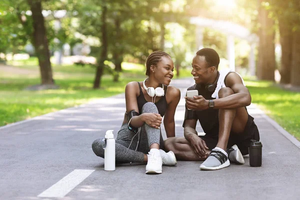 Χαρούμενο μαύρο αθλητικό ζευγάρι χαλαρώνοντας στο μονοπάτι στο πάρκο μετά την προπόνηση — Φωτογραφία Αρχείου