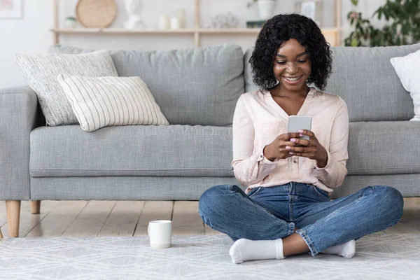 Evde boş zaman. Mutlu Siyah Kadın Akıllı Telefon ve Çayla Dinleniyor — Stok fotoğraf