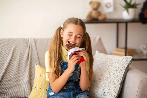 Chica comiendo chocolate sentado en un sofá en casa —  Fotos de Stock