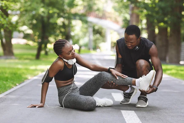 Cura nero uomo massaggio ferito gamba di fidanzata dopo running insieme all'aperto — Foto Stock