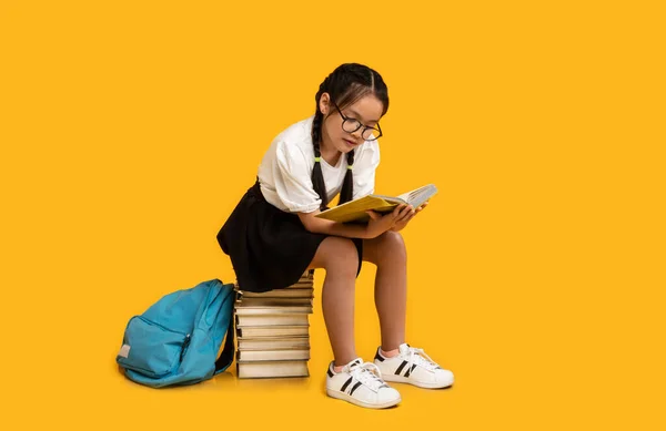 Japans schoolmeisje lezen boek doen huiswerk zitten over gele achtergrond — Stockfoto