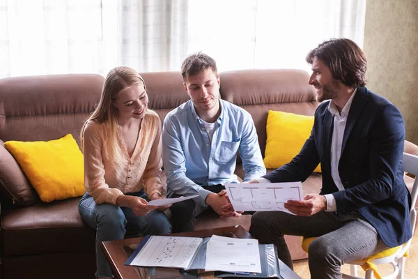 Makelar rumah yang percaya diri menunjukkan rencana rumah kepada beberapa calon pembeli di dalam ruangan — Stok Foto