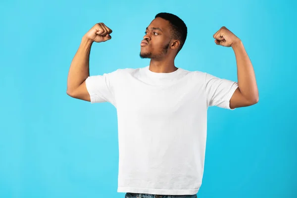 Fuerte hombre afroamericano mostrando bíceps de pie sobre fondo azul — Foto de Stock