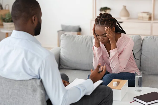 Individual psychotherapy. Depressed black woman sitting on couch at counselors office — Stock Photo, Image