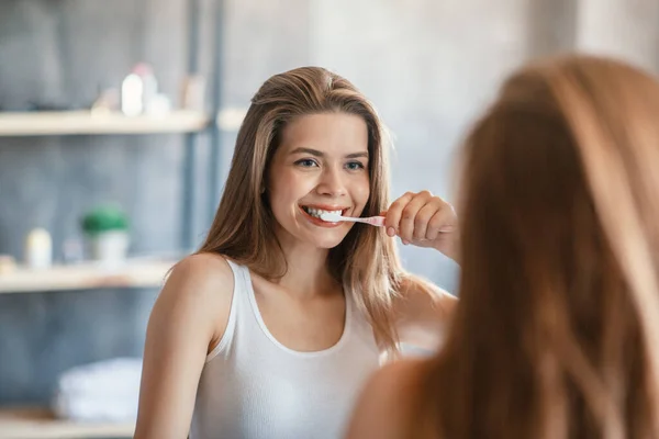 素敵な若いです女性ともに美しいです笑顔ブラッシング彼女の歯でミラーの前にバスルーム — ストック写真