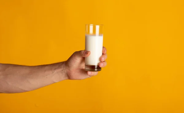 Millennial man holding glass of milk on orange background, close up of hand — Foto Stock
