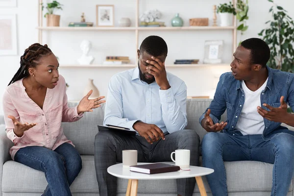 Desesperado conselheiro familiar sentado no sofá entre argumentando casal em seu escritório — Fotografia de Stock