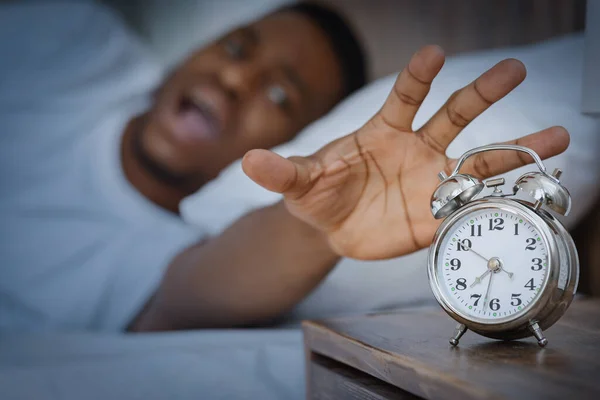 Schwarzer Kerl schaltet Wecker aus und schreit im Bett liegend — Stockfoto