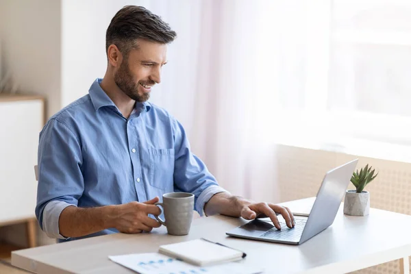 Innenministerium. Lächelnder Freiberufler checkt E-Mails am Laptop und trinkt Kaffee — Stockfoto