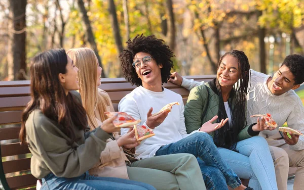 Jóvenes amigos internacionales comiendo pizza juntos en el parque —  Fotos de Stock