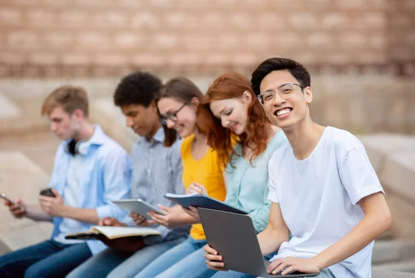 Azjatycki Student Learning with Coursemates siedzi poza budynkiem uniwersytetu — Zdjęcie stockowe