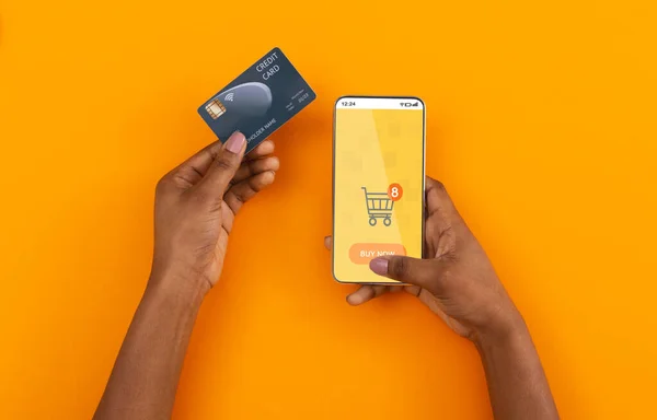 Hands Holding τηλέφωνο και πιστωτικές κάρτες αγορές σε απευθείας σύνδεση, πορτοκαλί φόντο — Φωτογραφία Αρχείου