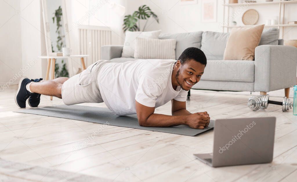 Black Man Exercising Doing Plank Exercise At Laptop Indoors