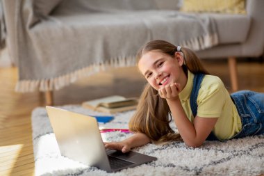 Halıda yatan ve bilgisayarını kullanan kız.