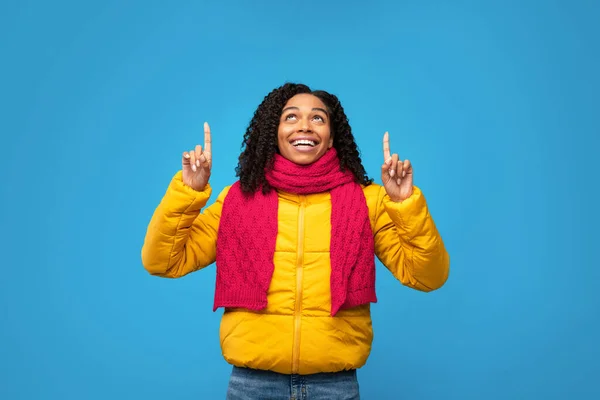 Mujer negra en chaqueta señalando los dedos hacia arriba sobre fondo azul —  Fotos de Stock