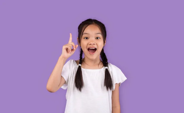 Petite fille asiatique pointant doigt vers le haut ayant une idée, fond violet — Photo