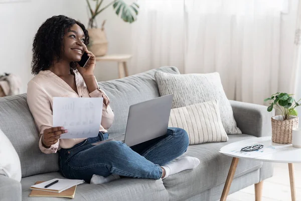Kvinna talar på mobilen och arbetar med papper och bärbar dator hemma — Stockfoto
