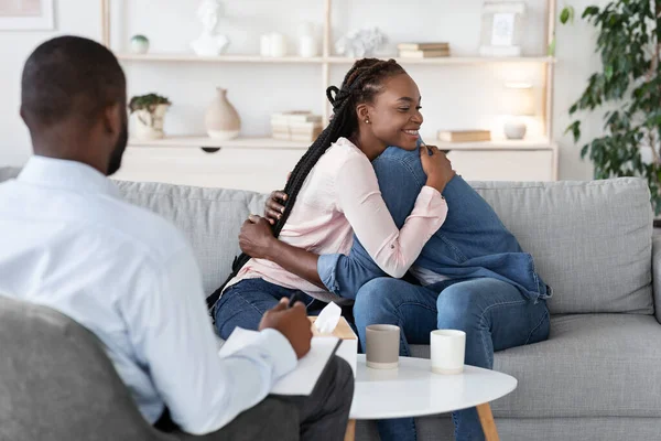 Terapia de pareja. Cónyuges africanos cariñosos abrazándose en la oficina de consejeros familiares después de la reconciliación —  Fotos de Stock