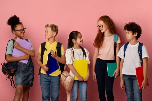 Schattige schoolkinderen van verschillende rassen en leeftijden kijken elkaar over pick achtergrond — Stockfoto