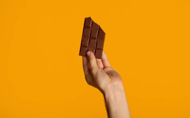 Turuncu arka planda çikolata tutan bin yıllık adamın yakın görüntüsü.